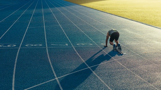 A runner prepares to begin a lap of a blue athletics track